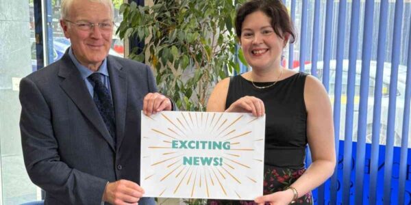 Directors of Woolliscrofts Solicitors holding 'exciting news' sign.