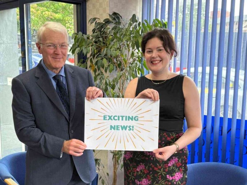 Directors of Woolliscrofts Solicitors holding 'exciting news' sign.